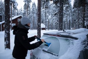 woman scraping snow and ice off of windshield during the winter