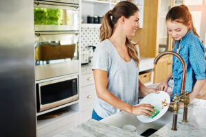 mother and child wash dishes at kitchen sink