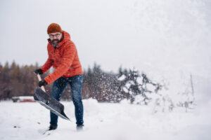 Man shoveling snow with shovel, cleaning driveway in front of the house. Scooping and throwing snow, shoveling.