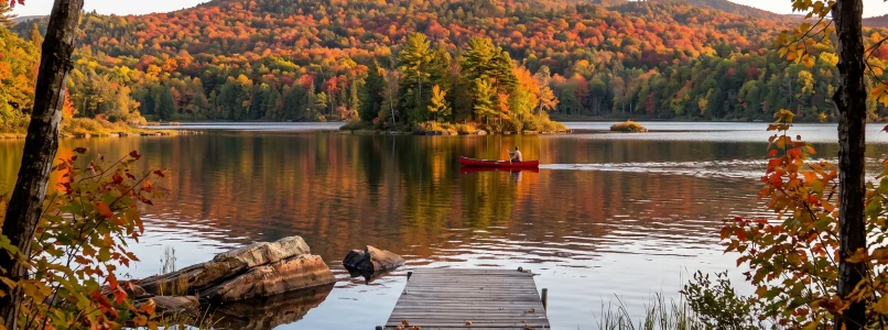 Scenic autumn lake landscape with a dock, red canoe, and vibrant foliage on mountains.